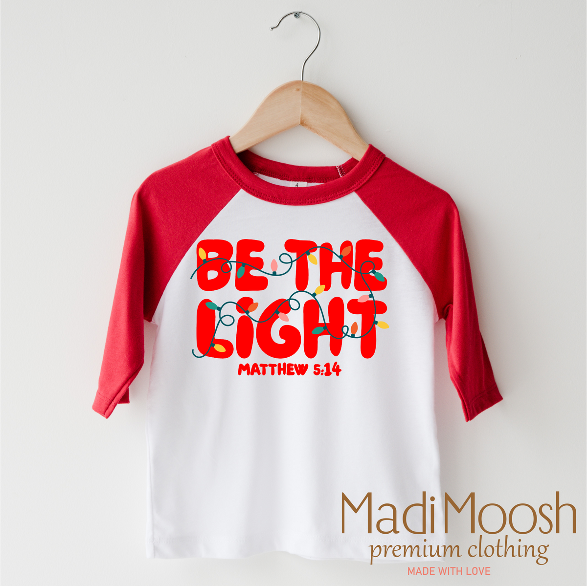 Be The Light Christmas design on a red-accented shirt.