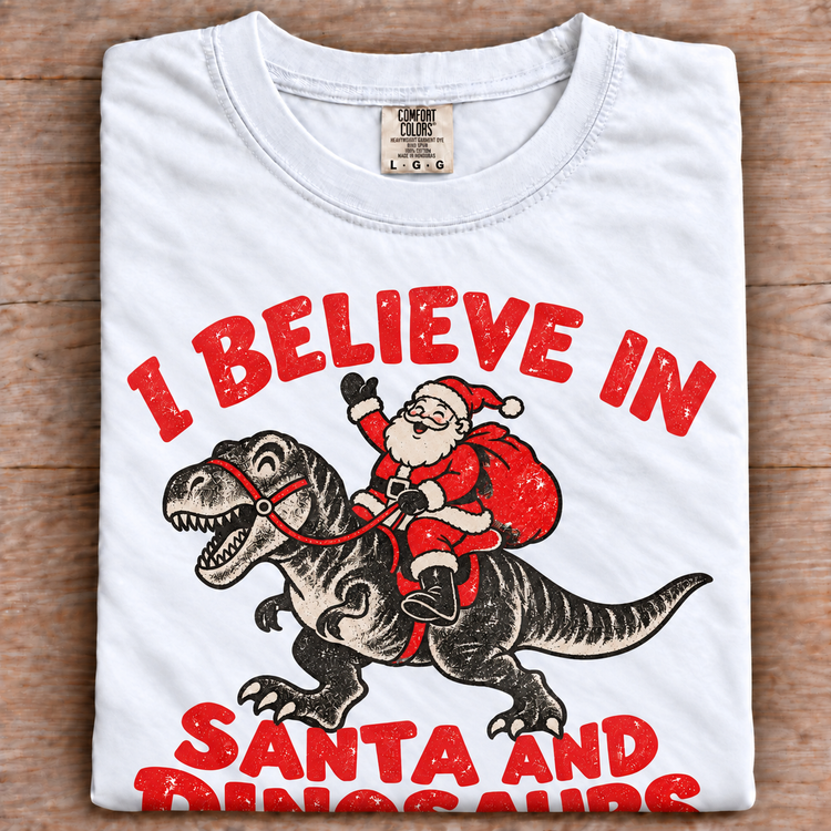 White Comfort Colors I Believe in Santa and Dinosaurs shirt folded on wood