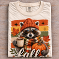 Natural Comfort Colors fall raccoon shirt with pumpkin and coffee graphic folded on wood