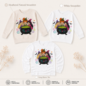 Natural and white sweatshirts and a white long-sleeve shirt featuring three witches around a bubbling cauldron with bats and stars.