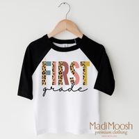 First Grade Leopard design on a raglan shirt with black sleeves.