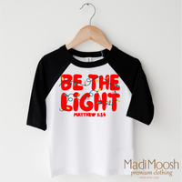 Be The Light Christmas design on a black-accented shirt.