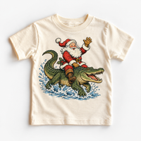 Santa riding an alligator Christmas design on a natural tee by Madi Moosh