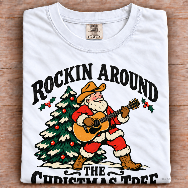 White Comfort Colors Rockin Around the Christmas Tree cowboy Santa shirt folded on wood