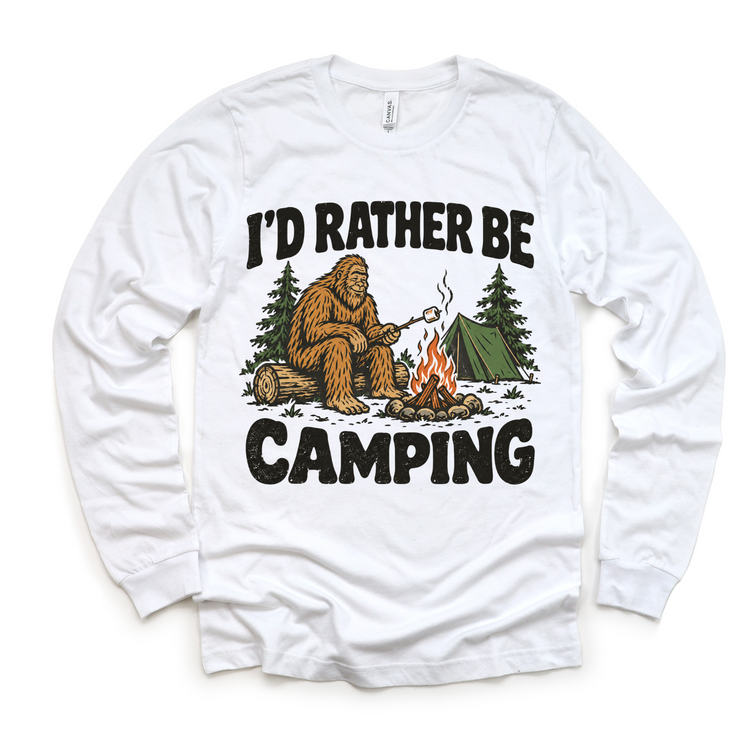 I'd Rather Be Camping Bigfoot roasting a marshmallow by a campfire on a white long sleeve tee
