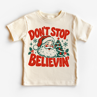 Don't Stop Believin' retro Santa and Christmas tree graphic in red and green on a natural short sleeve tee