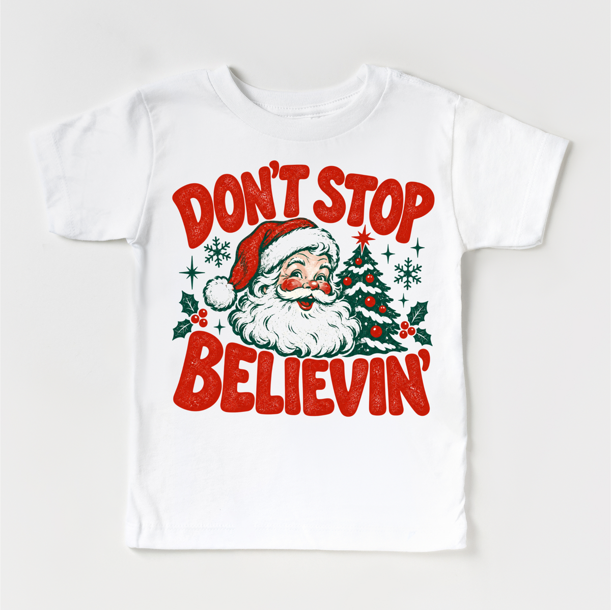 Don't Stop Believin' retro Santa and Christmas tree graphic in red and green on a white short sleeve tee