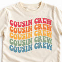 Close-up of the five-color wavy Cousin Crew graphic and neckline on a natural cotton tee.