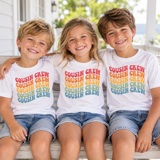 Three children wearing matching white Cousin Crew Wavy shirts on a sunny cottage porch.