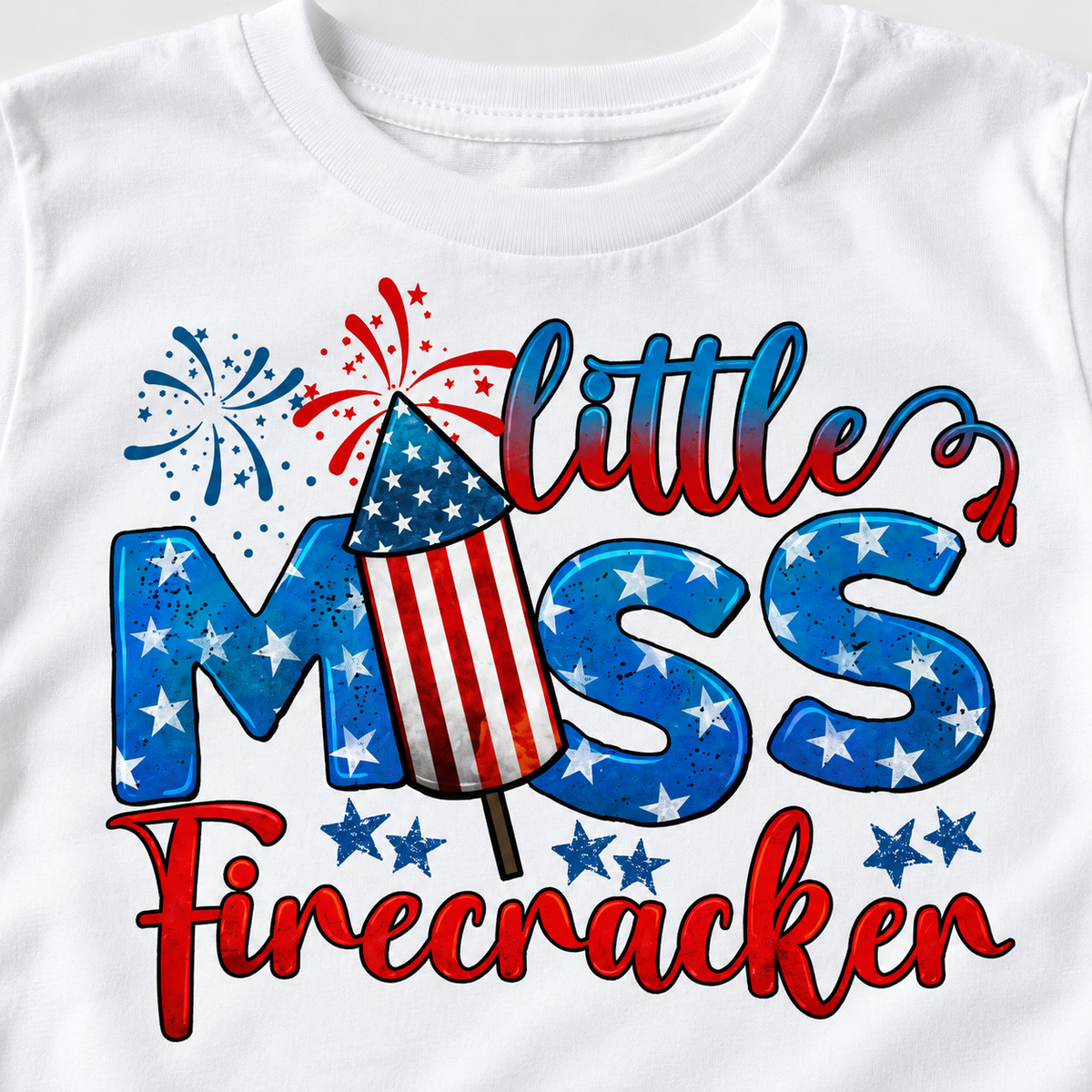 Close-up of Little Miss Firecracker lettering, stars and striped rocket artwork on a white cotton tee.