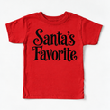Santa's Favorite Christmas shirt features elegant black lettering with curled details. Shown on red tee, front view.