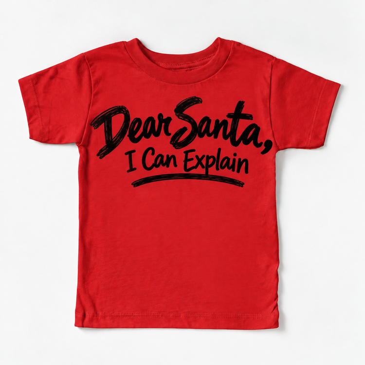 Dear Santa I Can Explain shirt features black brush lettering and a sweeping underline. Shown on red tee, front view.