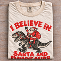 Natural Comfort Colors I Believe in Santa and Dinosaurs shirt folded on wood