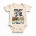 Someone in North Dakota Loves Me design on a natural beige baby bodysuit