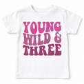 White Young Wild and Three girls birthday tee laid flat with the full pink and mauve design visible.