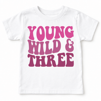 White Young Wild and Three girls birthday tee laid flat with the full pink and mauve design visible.